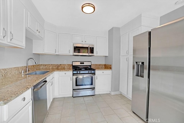 kitchen with white cabinets, appliances with stainless steel finishes, sink, light stone counters, and light tile patterned floors