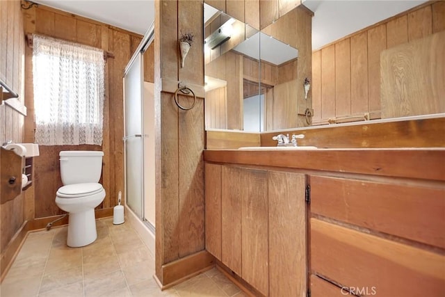 bathroom featuring a shower with door, toilet, vanity, and wooden walls