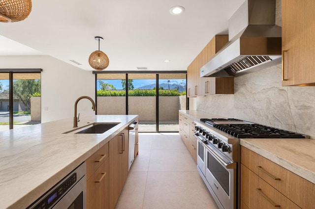 kitchen featuring sink, tasteful backsplash, high end range, decorative light fixtures, and wall chimney range hood