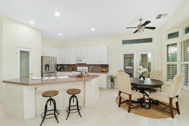 kitchen with white appliances, a kitchen breakfast bar, an island with sink, white cabinets, and french doors