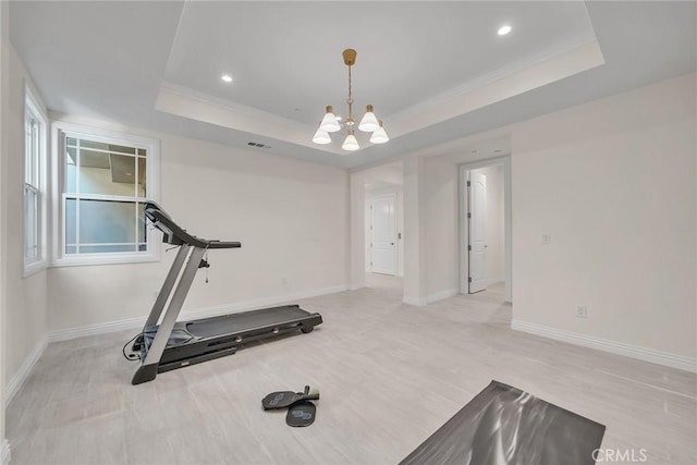 exercise area featuring a raised ceiling and a notable chandelier