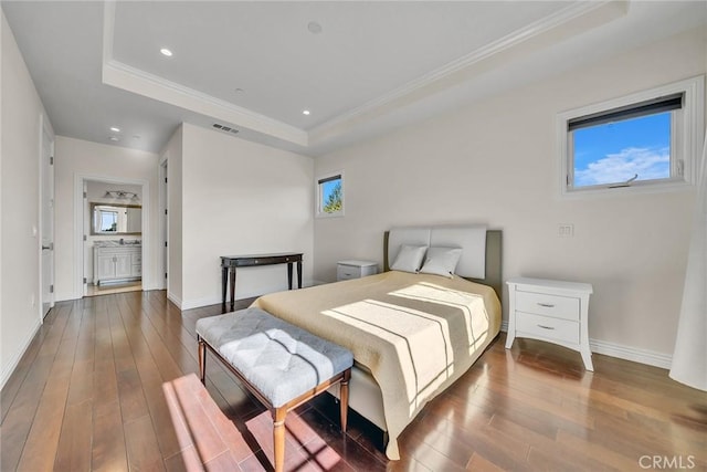 bedroom featuring dark hardwood / wood-style flooring, ornamental molding, a tray ceiling, and ensuite bath