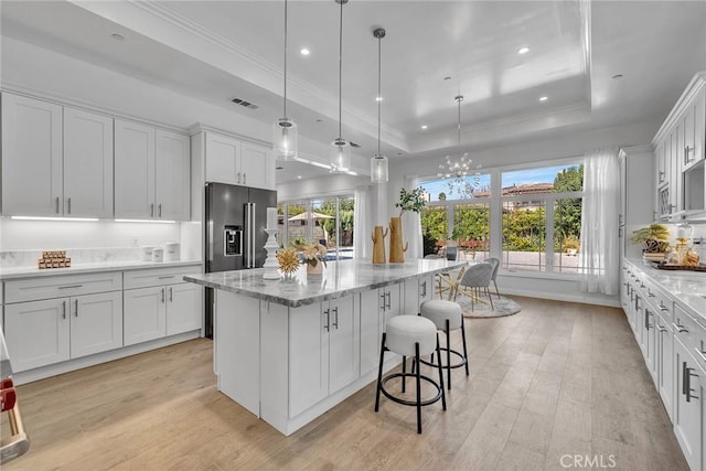 kitchen with light stone countertops, a center island, decorative light fixtures, white cabinetry, and a tray ceiling