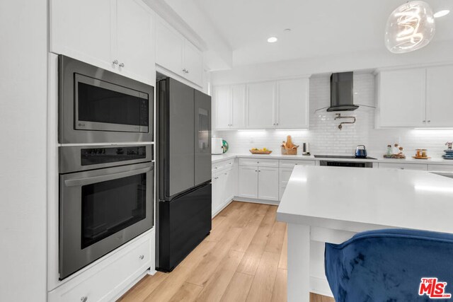 kitchen with appliances with stainless steel finishes, tasteful backsplash, decorative light fixtures, wall chimney range hood, and white cabinets