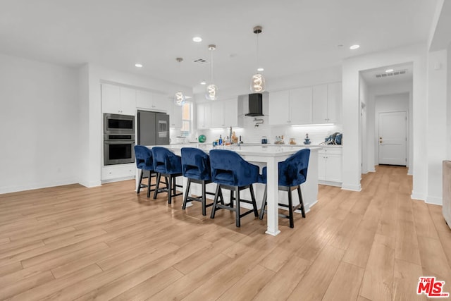 kitchen with a large island with sink, pendant lighting, white cabinetry, stainless steel appliances, and wall chimney exhaust hood