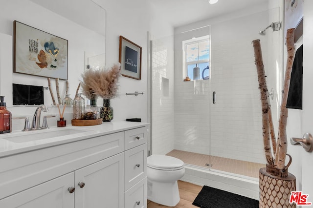 bathroom featuring toilet, vanity, an enclosed shower, and hardwood / wood-style floors