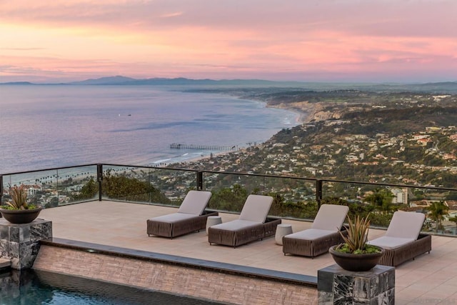 patio terrace at dusk featuring a balcony and a water view