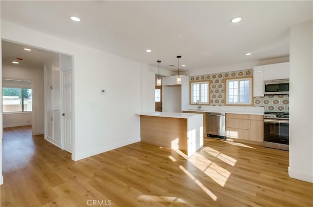 kitchen with appliances with stainless steel finishes, white cabinetry, tasteful backsplash, hanging light fixtures, and light hardwood / wood-style flooring