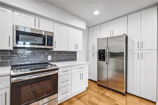 kitchen featuring light wood-type flooring, appliances with stainless steel finishes, decorative backsplash, and white cabinets