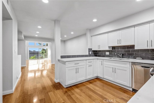 kitchen featuring tasteful backsplash, stainless steel dishwasher, sink, white cabinetry, and light wood-type flooring