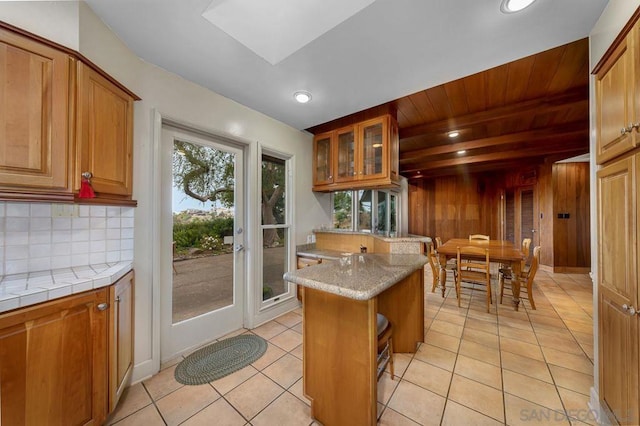 kitchen featuring decorative backsplash, wooden ceiling, light tile patterned floors, and wooden walls