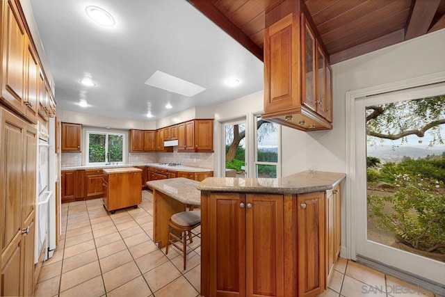 kitchen featuring a skylight, kitchen peninsula, decorative backsplash, a kitchen breakfast bar, and light stone countertops