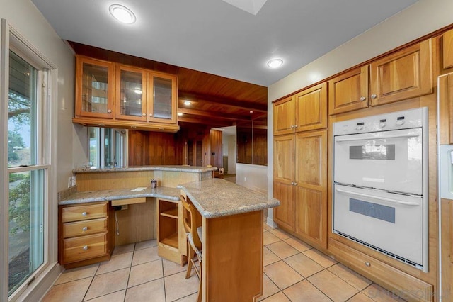 kitchen with white double oven, light stone counters, kitchen peninsula, and light tile patterned flooring