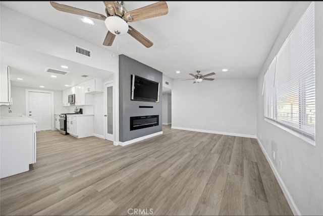 unfurnished living room with light wood-type flooring, ceiling fan, and sink