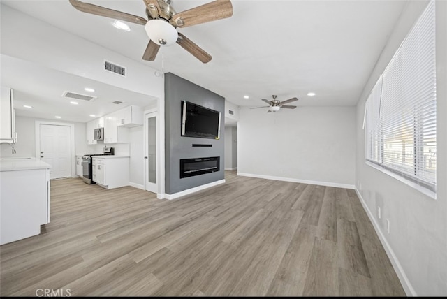 unfurnished living room featuring ceiling fan, sink, and light wood-type flooring