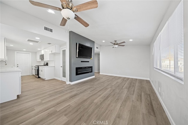 unfurnished living room with ceiling fan, sink, and light hardwood / wood-style floors