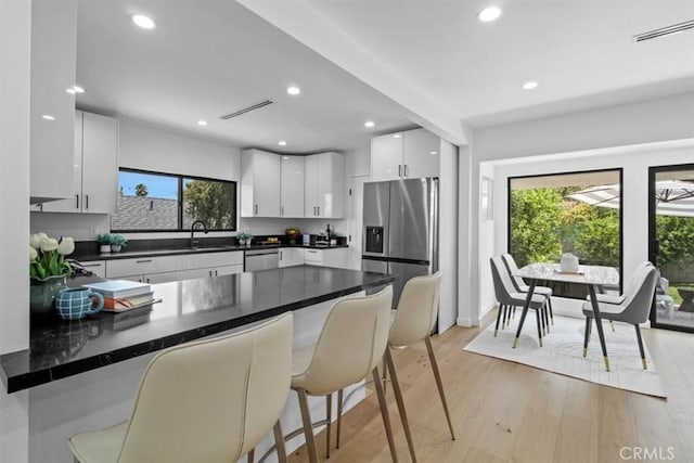 kitchen with light hardwood / wood-style floors, kitchen peninsula, a kitchen bar, stainless steel appliances, and white cabinets