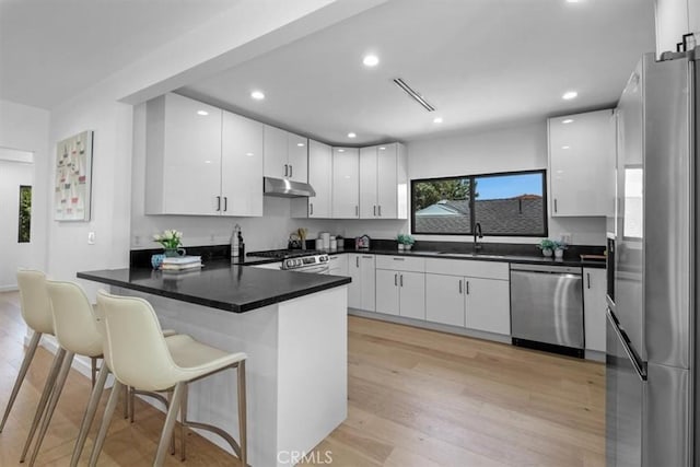 kitchen featuring white cabinetry, a kitchen bar, kitchen peninsula, stainless steel appliances, and sink