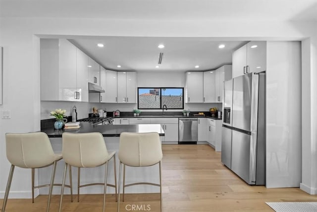 kitchen with a breakfast bar, sink, light wood-type flooring, stainless steel appliances, and white cabinets