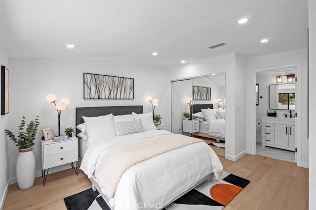 bedroom featuring light wood-type flooring, a closet, ensuite bathroom, and vaulted ceiling