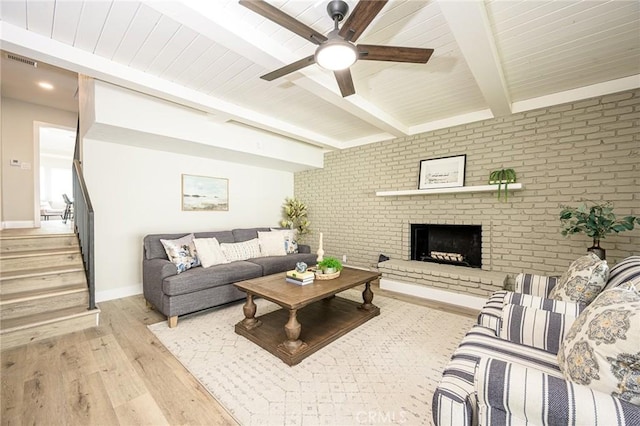 living room with a brick fireplace, ceiling fan, light wood-type flooring, brick wall, and beamed ceiling