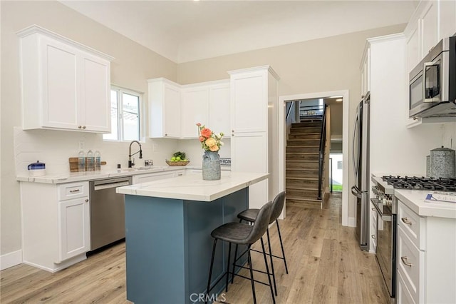 kitchen featuring white cabinetry, stainless steel appliances, light wood-type flooring, a kitchen island, and sink