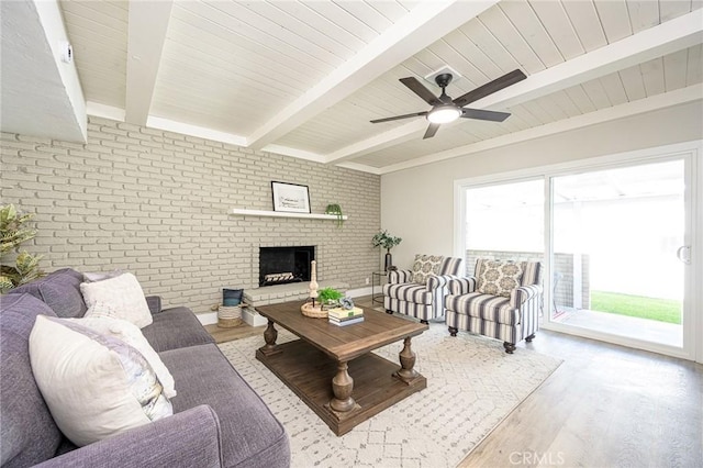 living room with brick wall, a healthy amount of sunlight, beam ceiling, and light hardwood / wood-style flooring