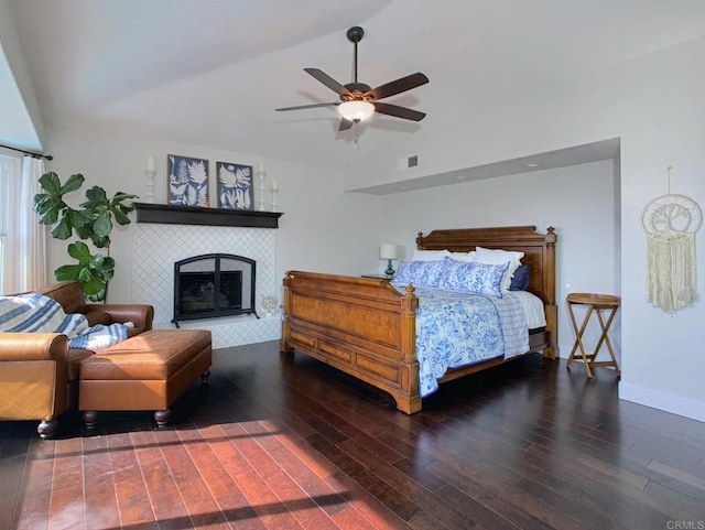 bedroom featuring ceiling fan, dark hardwood / wood-style flooring, lofted ceiling, and a tile fireplace