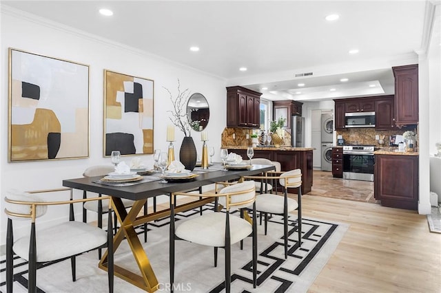 dining room featuring light hardwood / wood-style floors, crown molding, and stacked washer and dryer