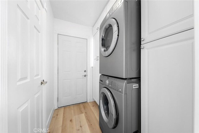 clothes washing area featuring cabinets, stacked washer / drying machine, and light wood-type flooring