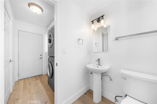 bathroom with toilet, stacked washer / drying machine, hardwood / wood-style flooring, and sink