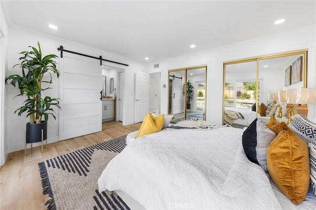 bedroom with light wood-type flooring, ensuite bathroom, crown molding, a barn door, and multiple closets