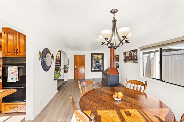 dining area with arched walkways, a notable chandelier, light wood-style flooring, and baseboards