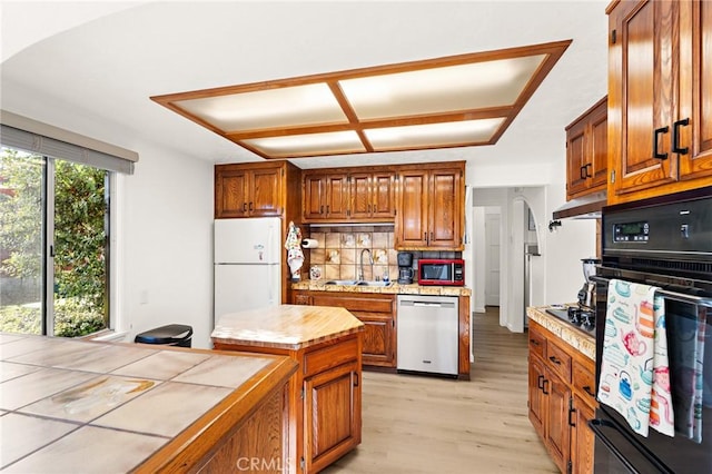 kitchen with oven, under cabinet range hood, stainless steel dishwasher, freestanding refrigerator, and a sink