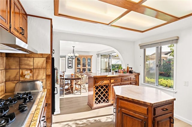 kitchen with a center island, stainless steel gas cooktop, tile countertops, light wood-type flooring, and a notable chandelier