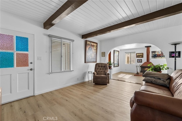 living area featuring baseboards, beam ceiling, arched walkways, wood ceiling, and light wood-style floors