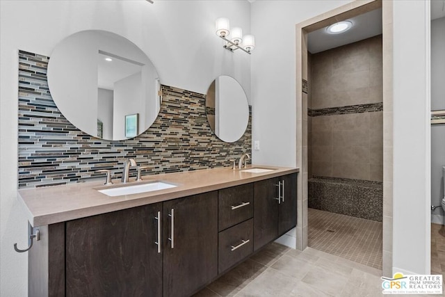 bathroom with tile patterned flooring, decorative backsplash, tiled shower, and vanity