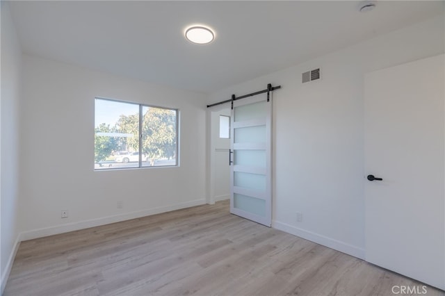 unfurnished bedroom with a barn door and light wood-type flooring