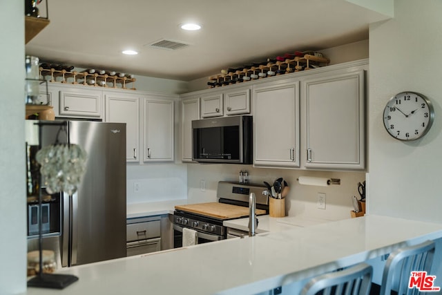 kitchen featuring white cabinetry, appliances with stainless steel finishes, a kitchen bar, and kitchen peninsula