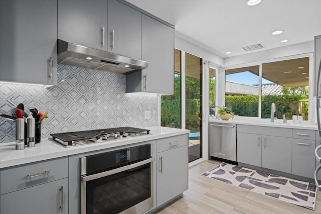 kitchen featuring stainless steel appliances, decorative backsplash, light hardwood / wood-style flooring, and gray cabinets