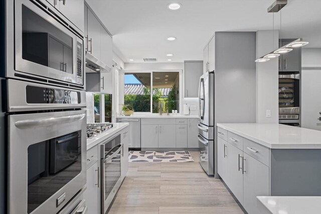 kitchen featuring decorative light fixtures, appliances with stainless steel finishes, gray cabinetry, and light hardwood / wood-style flooring