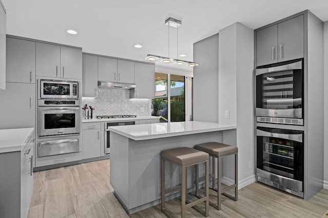 kitchen featuring a breakfast bar, kitchen peninsula, appliances with stainless steel finishes, gray cabinetry, and beverage cooler