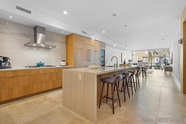 kitchen featuring wall chimney exhaust hood, paneled built in refrigerator, a kitchen bar, a large island with sink, and sink