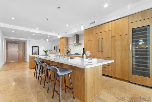 kitchen featuring beverage cooler, hanging light fixtures, light stone counters, wall chimney exhaust hood, and a spacious island