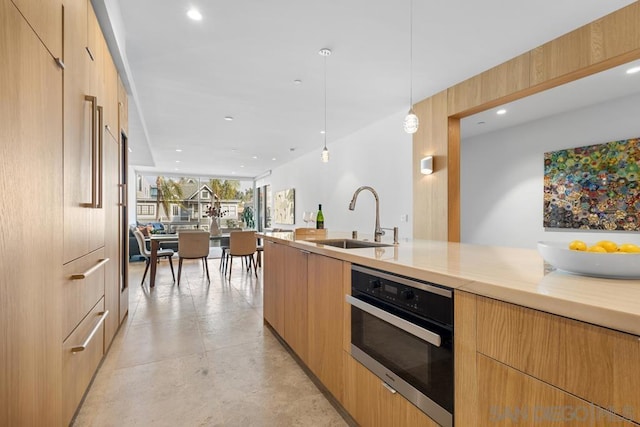 kitchen featuring decorative light fixtures, oven, light brown cabinets, and sink