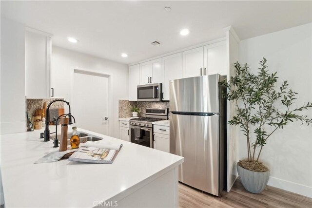 kitchen with backsplash, sink, white cabinetry, light wood-type flooring, and appliances with stainless steel finishes