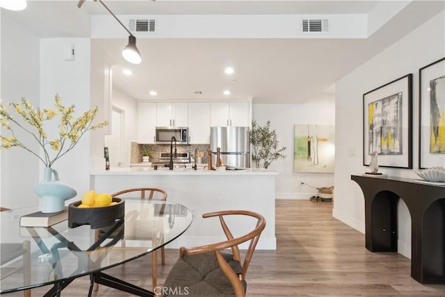 kitchen featuring white cabinetry, stainless steel appliances, decorative backsplash, kitchen peninsula, and light wood-type flooring