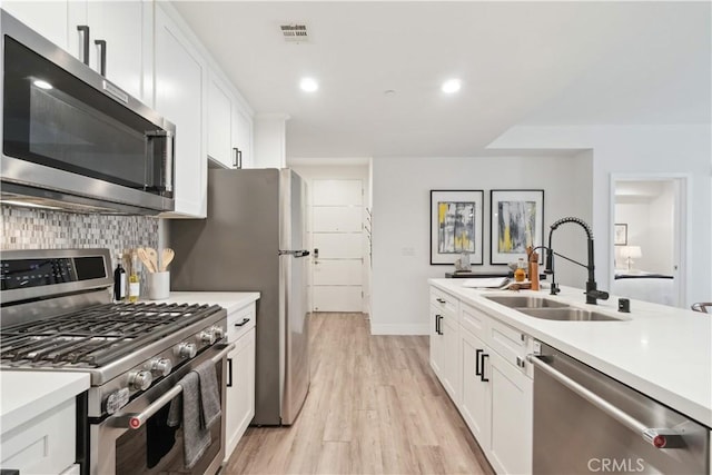 kitchen featuring white cabinetry, stainless steel appliances, decorative backsplash, light hardwood / wood-style flooring, and sink