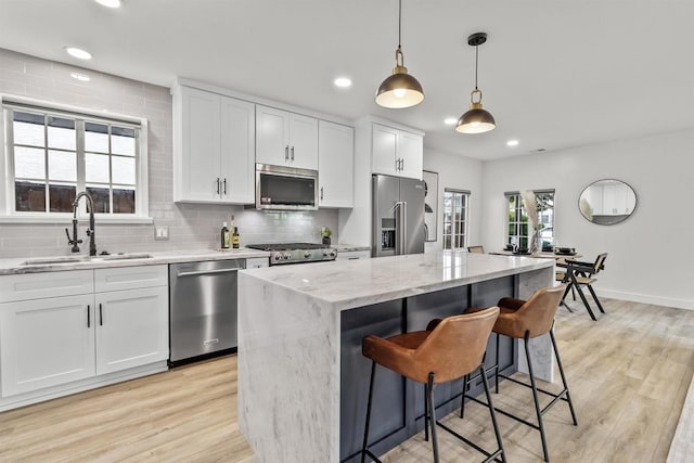 kitchen featuring stainless steel appliances, white cabinets, a kitchen island, light stone counters, and sink