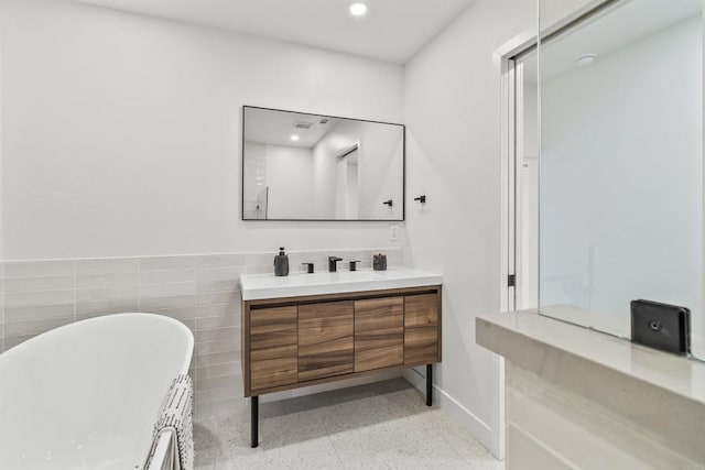 bathroom with a washtub, tile walls, and vanity